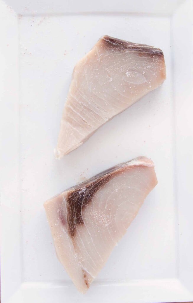 two swordfish steaks salted on a white platter