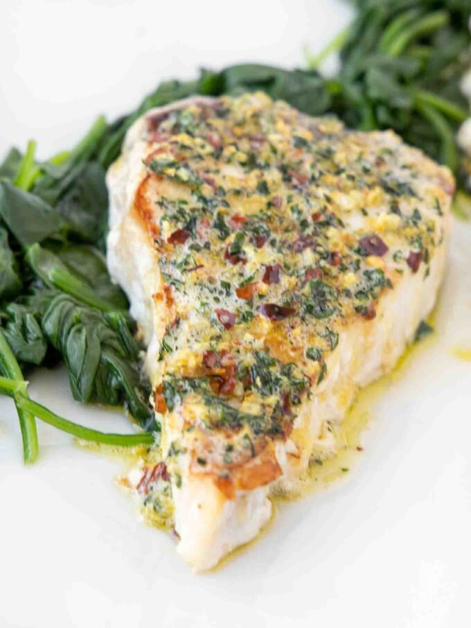 overhead view of a pan roasted swordfish steak topped with garlic ginger topping on a bed of spinach on a white platter