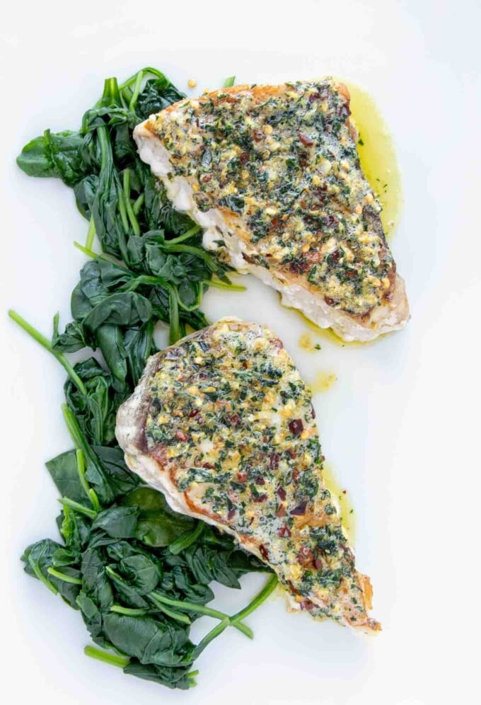 overhead view of two pan roasted swordfish steaks topped with garlic ginger topping on a bed of spinach on a white platter