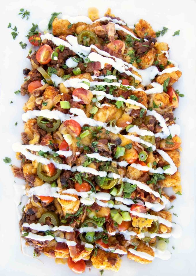 overhead shot of loaded tater tot nachos on a white platter