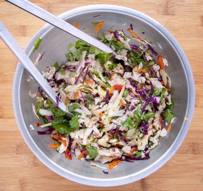 Asian slaw in a stainless steel bowl with tongs