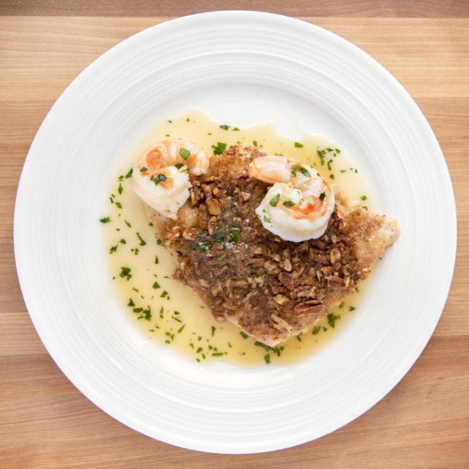 overhead view of pecan encrusted red snapper with shrimp and margarita sauce on a white plate