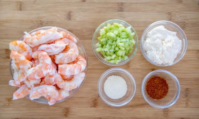 ingredients to make shrimp salad in bowls on a cutting board