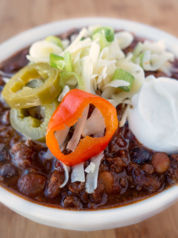 four bean chili in a white bowl topped with cheese jalapenos and sour cream