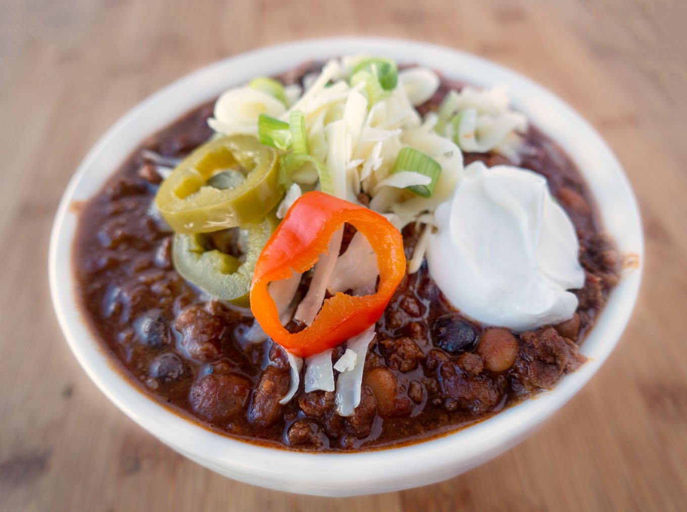 four bean chili in a white bowl topped with cheese jalapenos and sour cream