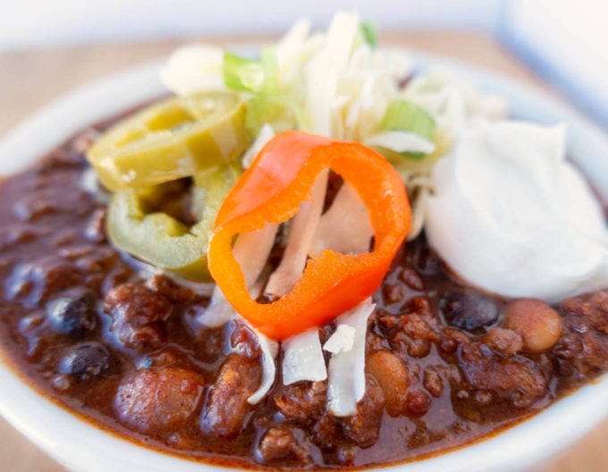 four bean chili in a white bowl topped with cheese jalapenos and sour cream