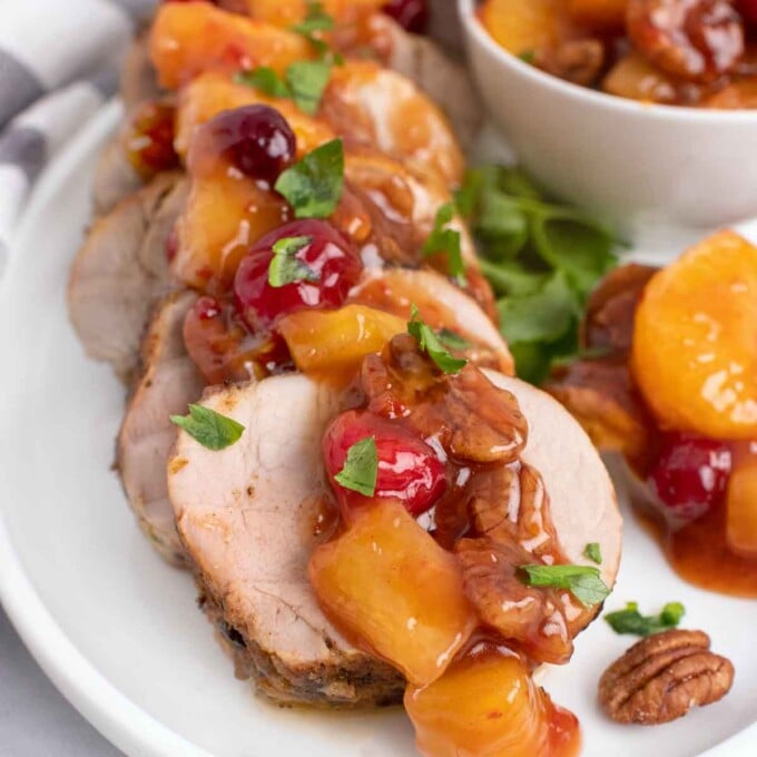 slices of peppered pork loin topped with the sweet chili pecan fruit sauce on a white plate