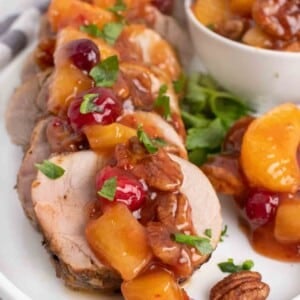 slices of peppered pork loin topped with the sweet chili pecan fruit sauce on a white plate