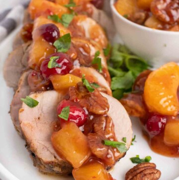 slices of peppered pork loin topped with the sweet chili pecan fruit sauce on a white plate