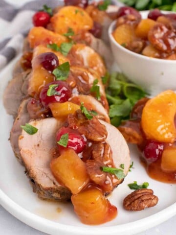 slices of peppered pork loin topped with the sweet chili pecan fruit sauce on a white plate