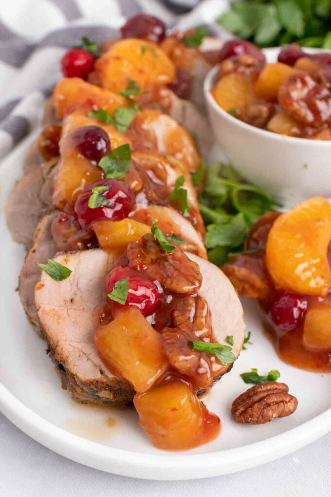 slices of peppered pork loin topped with the sweet chili pecan fruit sauce on a white plate
