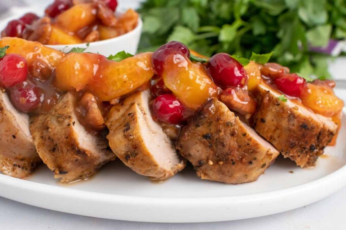 side view of slices of peppered pork loin topped with the sweet chili pecan fruit sauce on a white plate