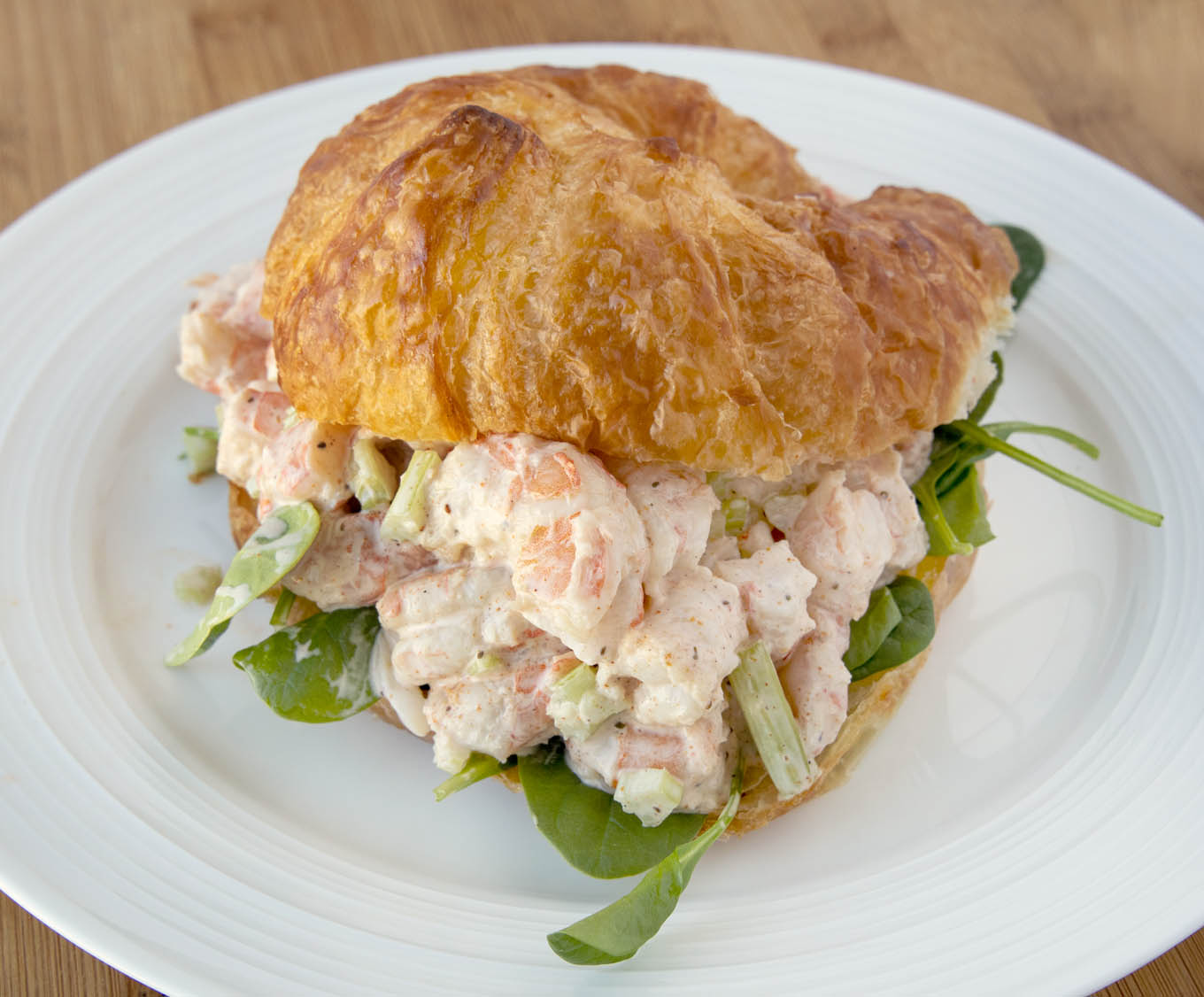 Shrimp salad with baby spinach on croissant on a white plate.