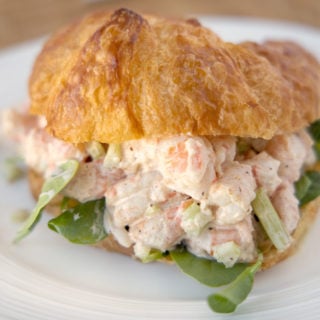 shrimp salad with baby spinach on croissant on a white plate
