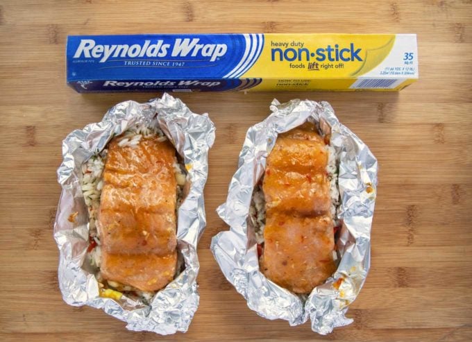 2 foil packets with mango bourbon salmon and a box of Reynolds wrap on a wooden cutting board