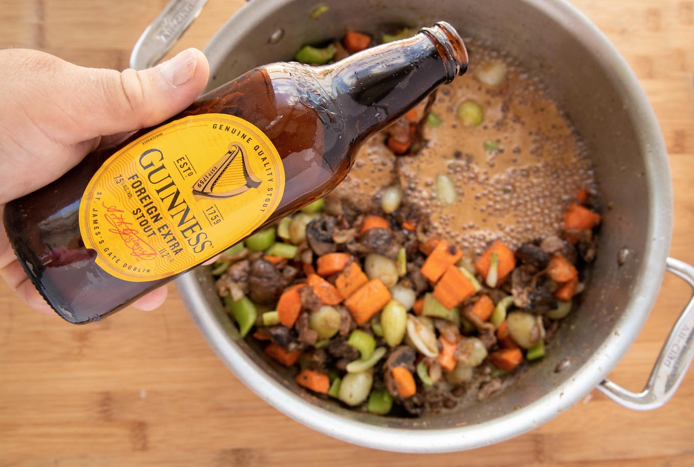 pouring a bottle of Guinness extra Stout into the pot of vegetables