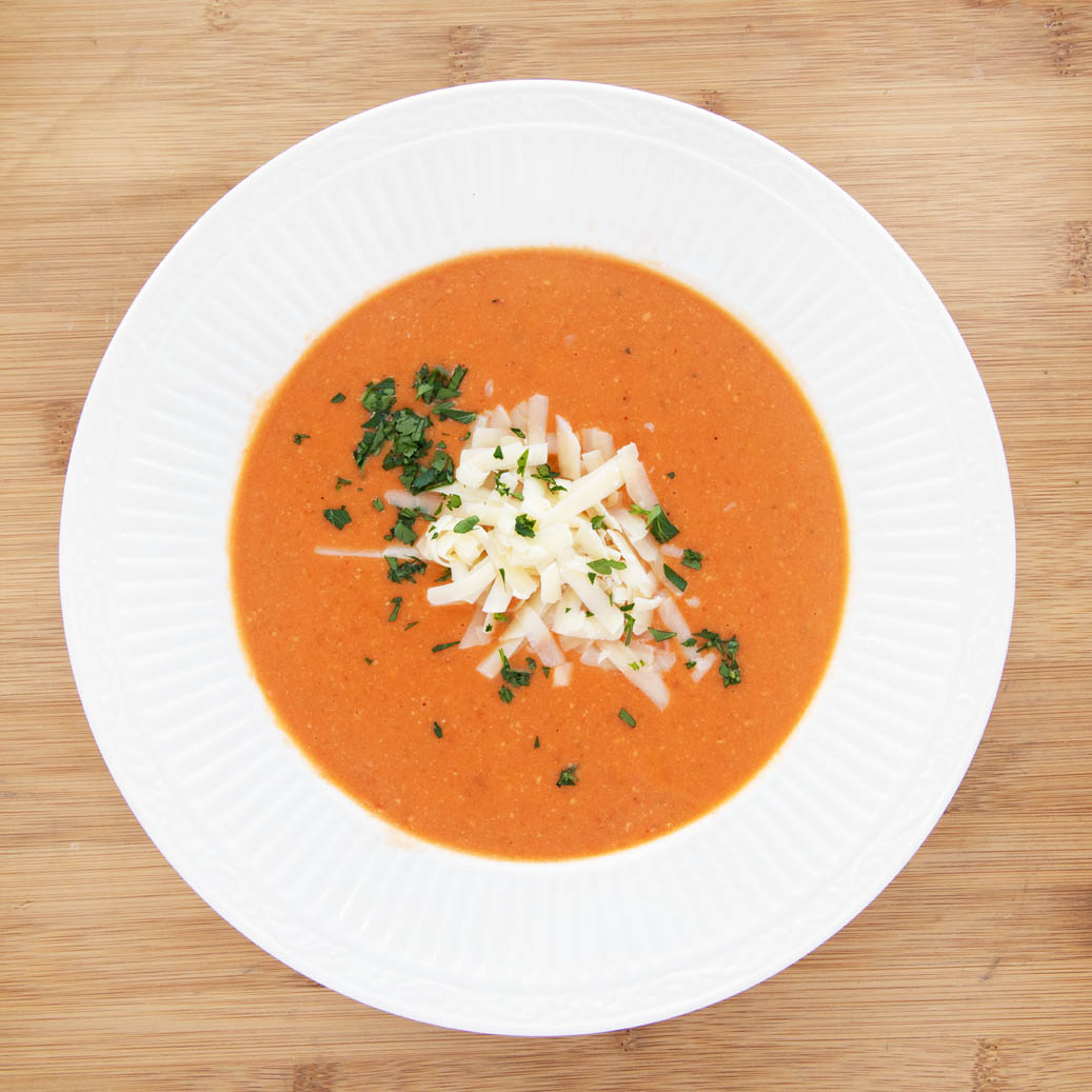 white bowl of tomato bisque with shredded cheddar and parsley garnish.