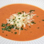 white bowl of tomato bisque with shredded cheddar and parsley garnish