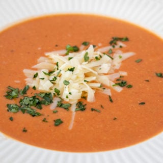 white bowl of tomato bisque with shredded cheddar and parsley garnish