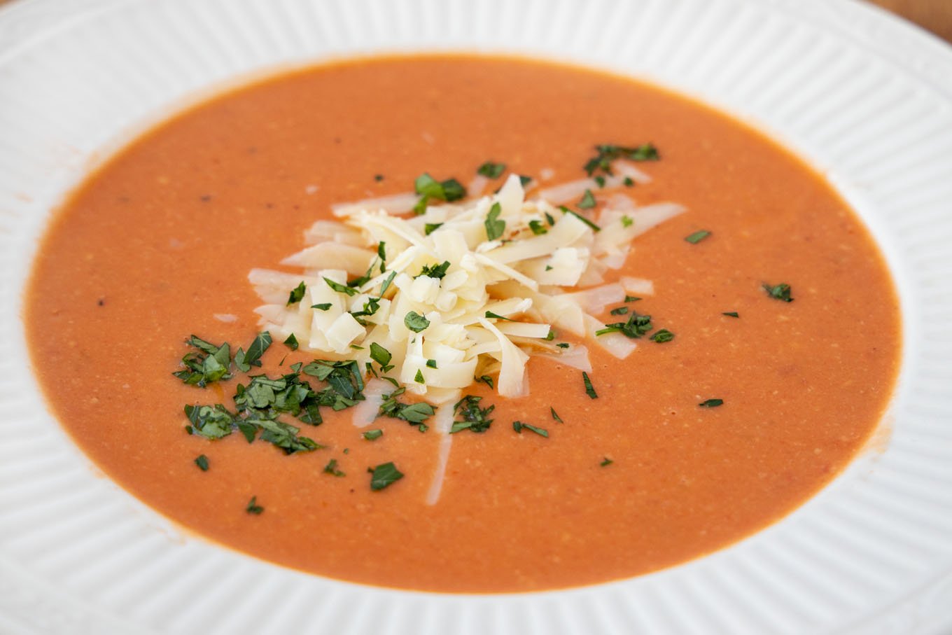 white bowl of tomato bisque with shredded cheddar and parsley garnish.