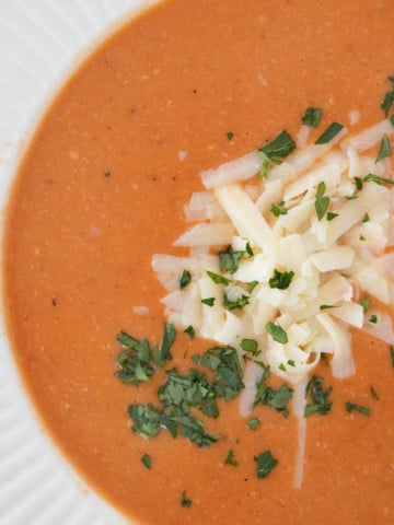 overhead shot of white bowl of tomato bisque with shredded cheddar and parsley garnish
