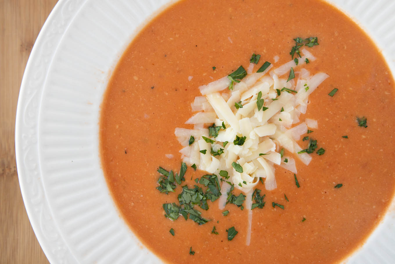 overhead shot of white bowl of tomato bisque with shredded cheddar and parsley garnish.