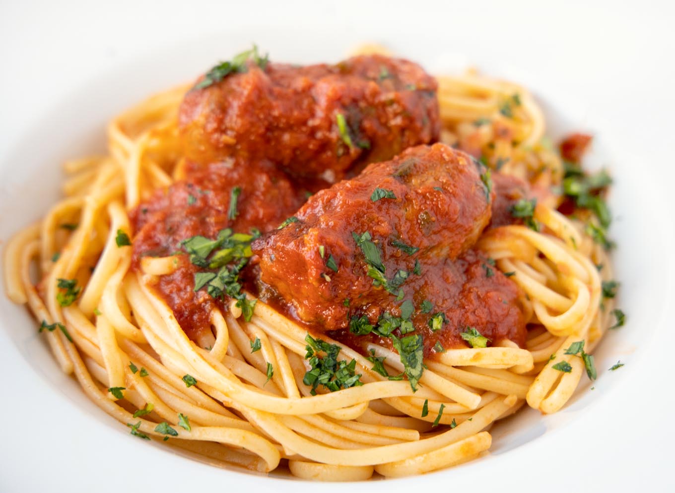 linguine and sausage with spaghetti sauce in a white bowl with sprinkled chopped parsley