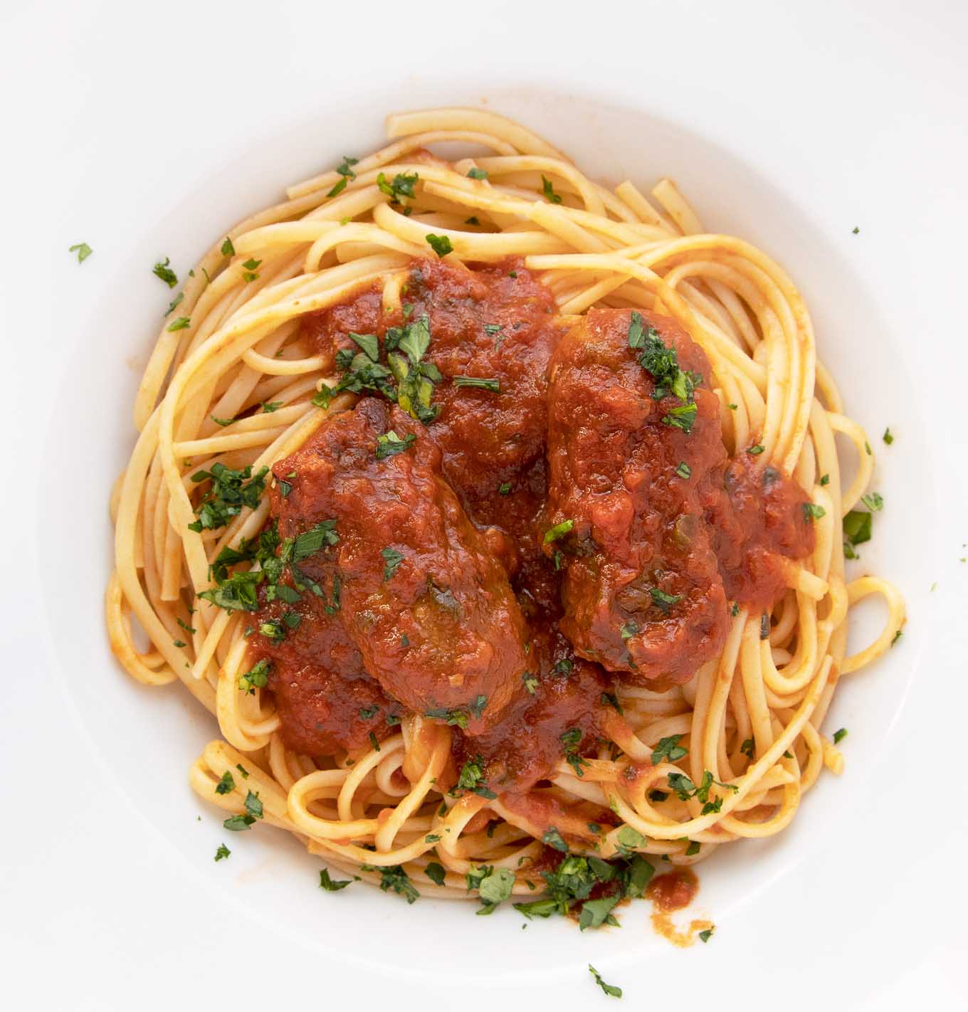 overhead shot of linguine and sausage with spaghetti sauce in a white bowl