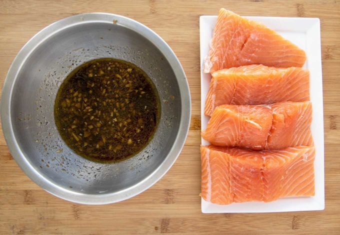 salmon filets on a white platter next to a stainless steel bowl with marinade