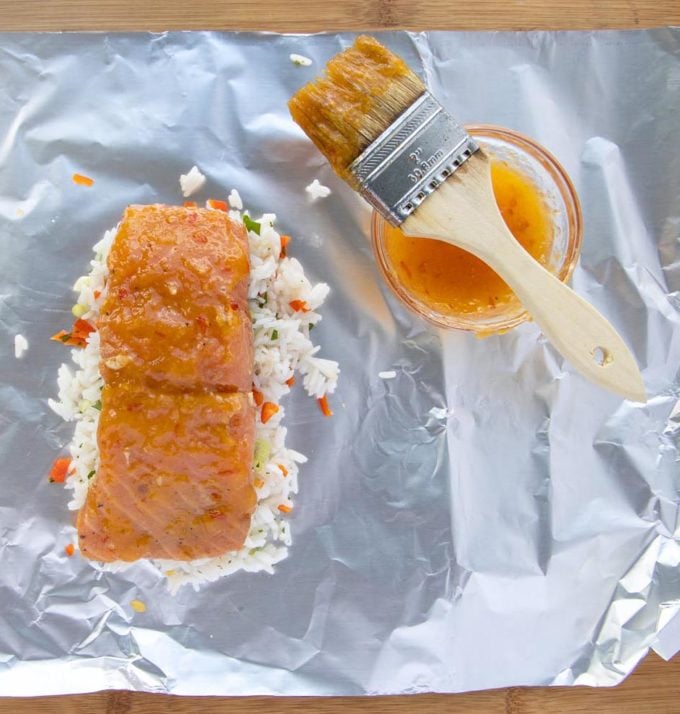 glazed mango bourbon salmon on rice on foil sheet with bowl of glaze and brush