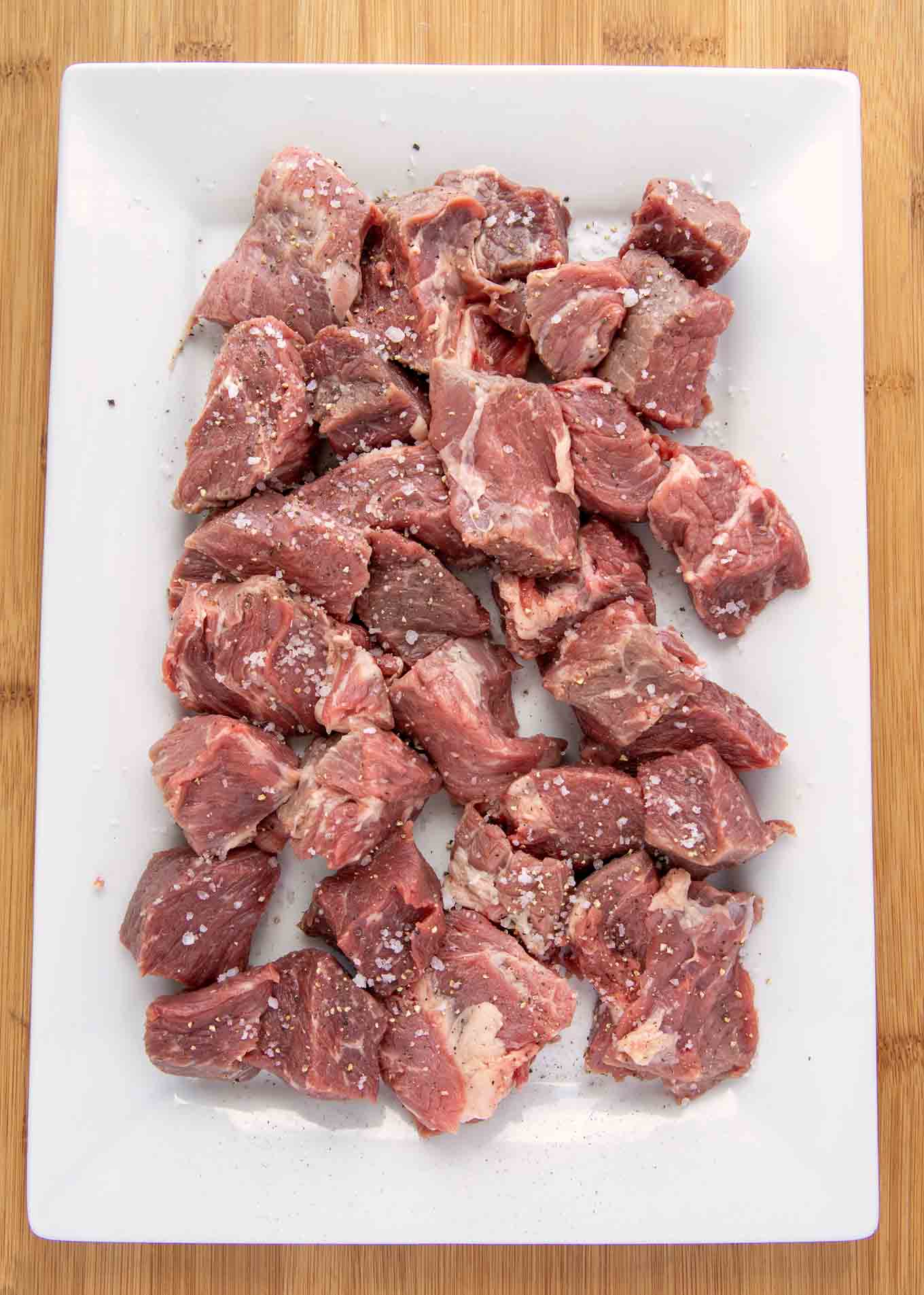 cubes of beef on a white oblong serving platter seasoned with sea salt an pepper