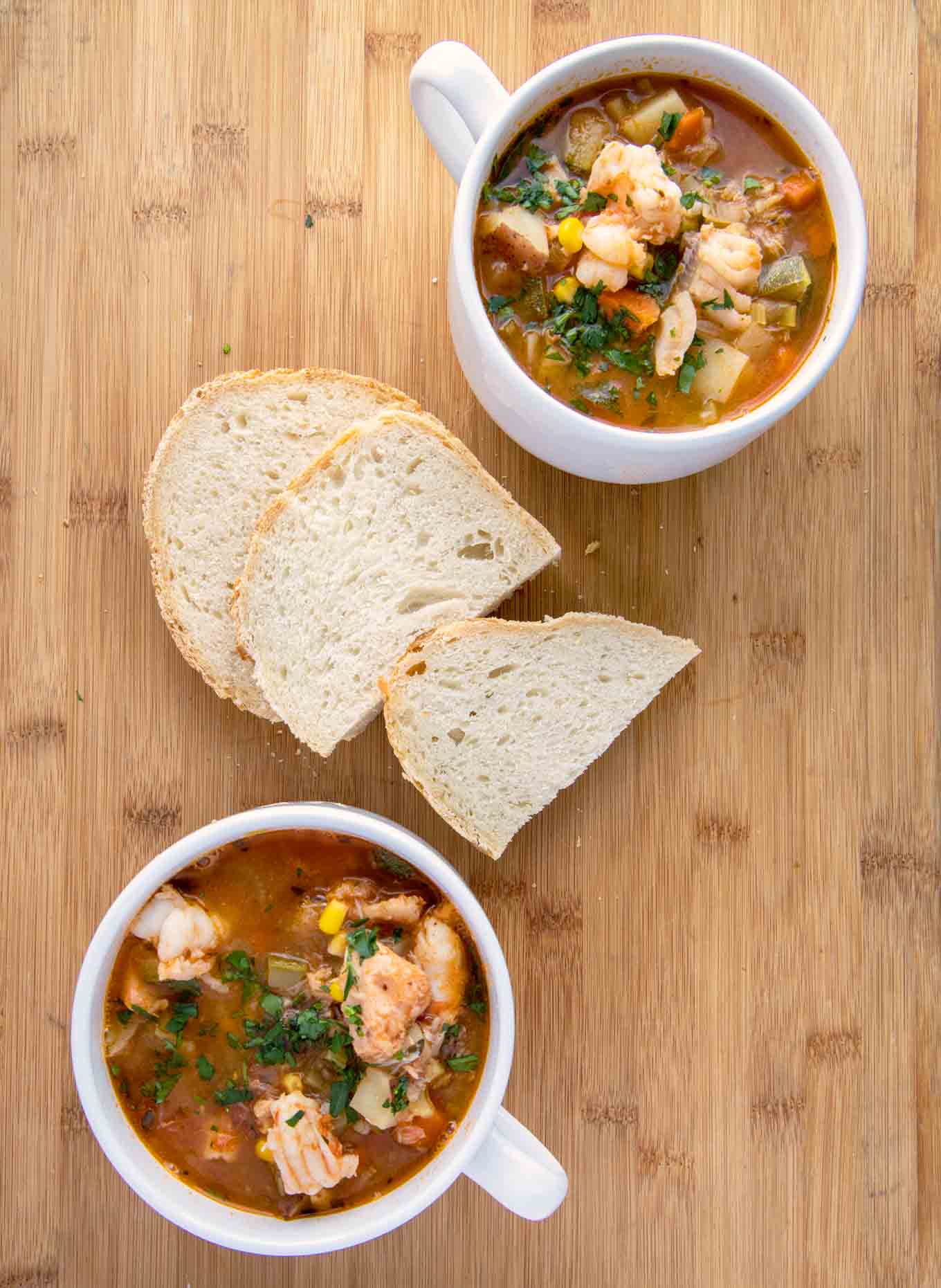 2 white cups of seafood soup with slices of bread on a wooden cutting board