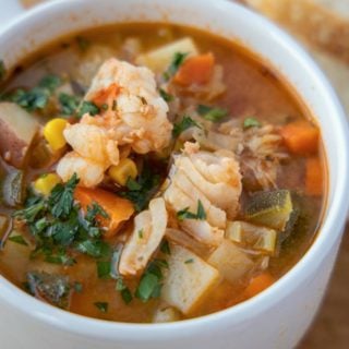 white cup of seafood soup with slices of bread in the background