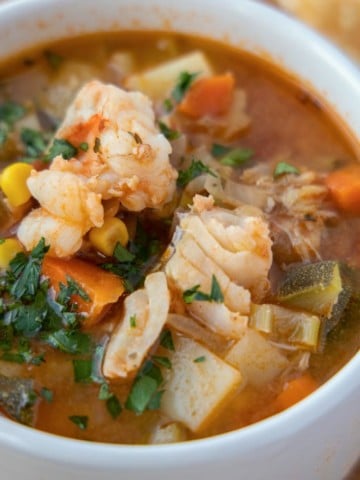 white cup of seafood soup with slices of bread in the background