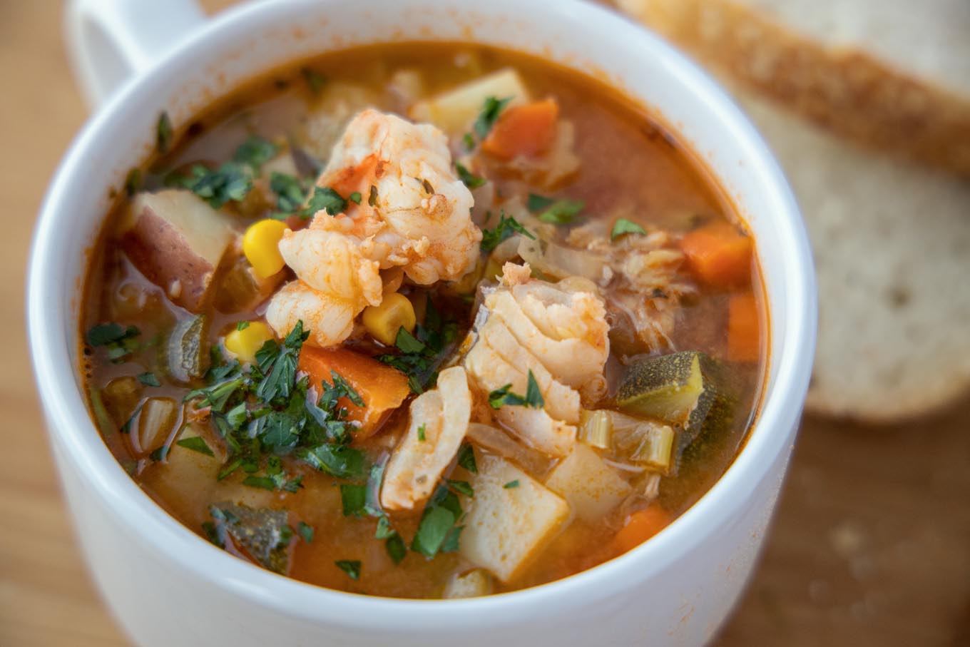 white cup of seafood soup with slices of bread in the background