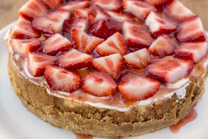 whole cheesecake topped with strawberries and glaze on a white plate