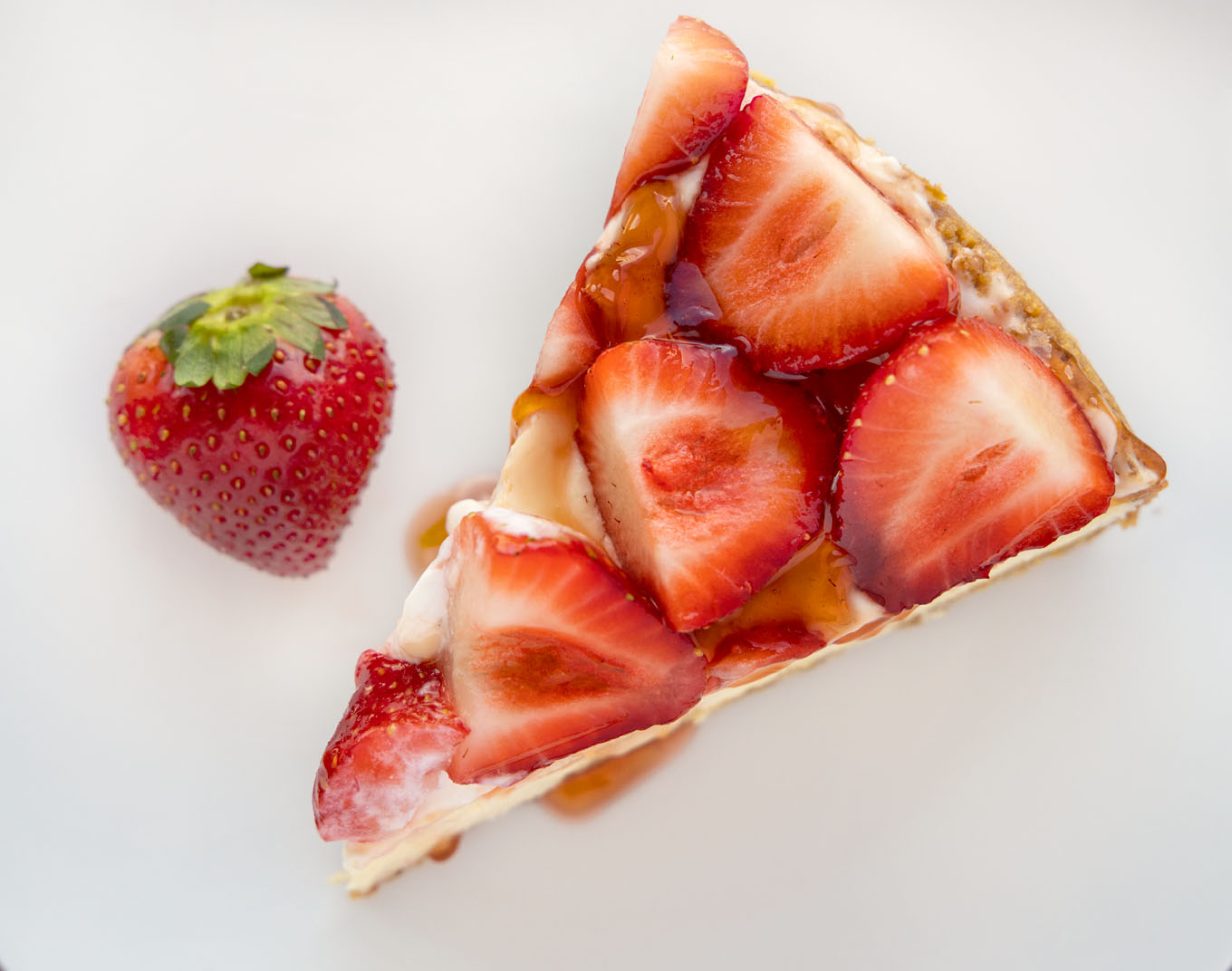overhead view of a slice of strawberry cheesecake on a white plate with a strawberry