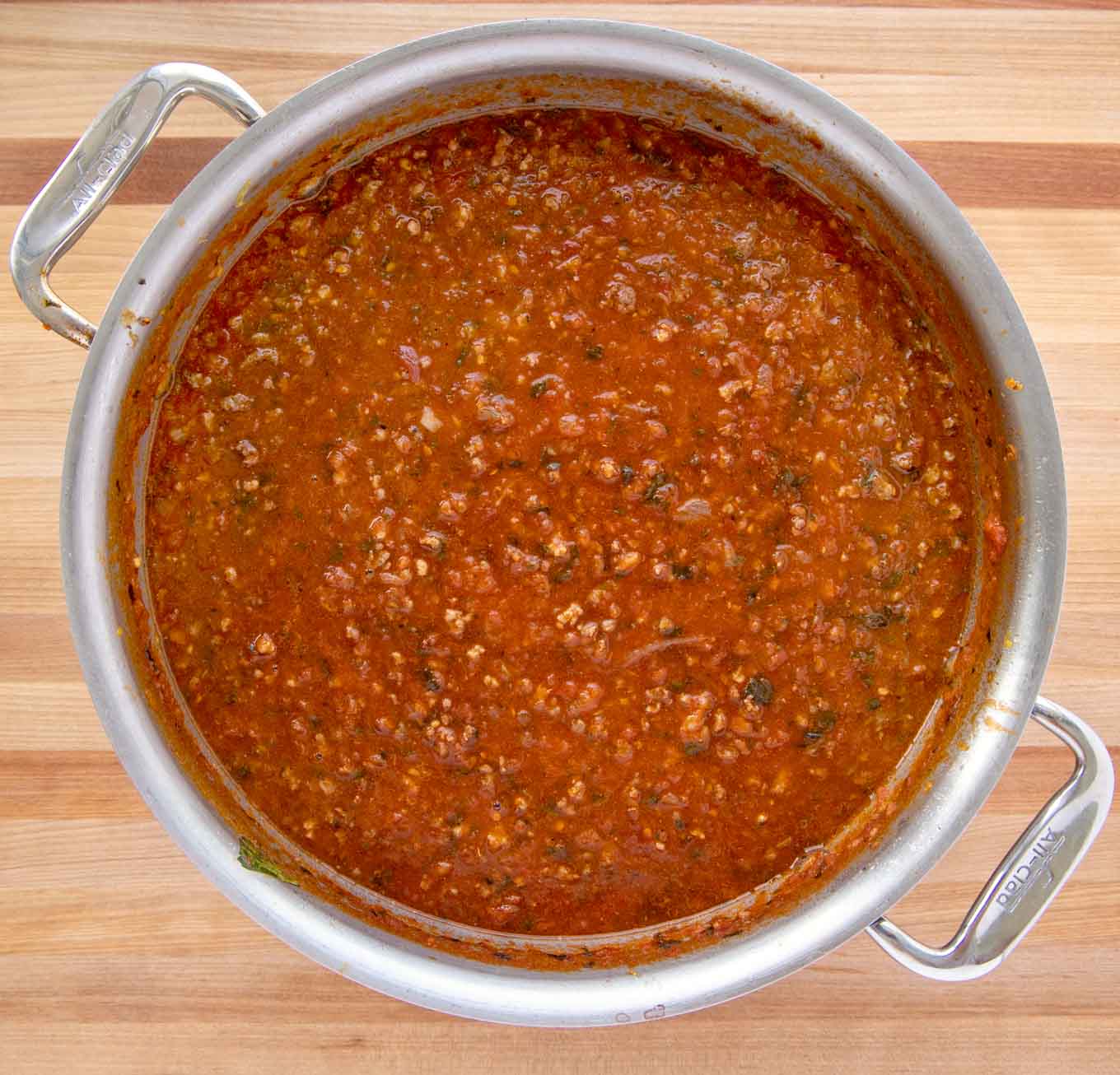 Tomatoes added to a large pot with cooked meats and soffritto.