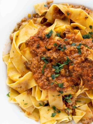 bolognese sauce served over pappardelle in a white bowl