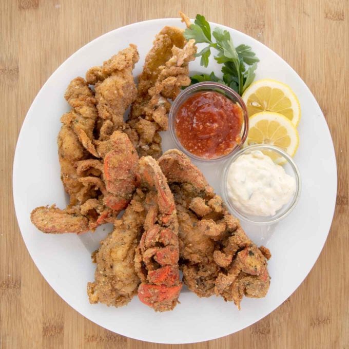 fried lobster tails on a white plate with lemon slices, cocktail sauce and tartar sauce