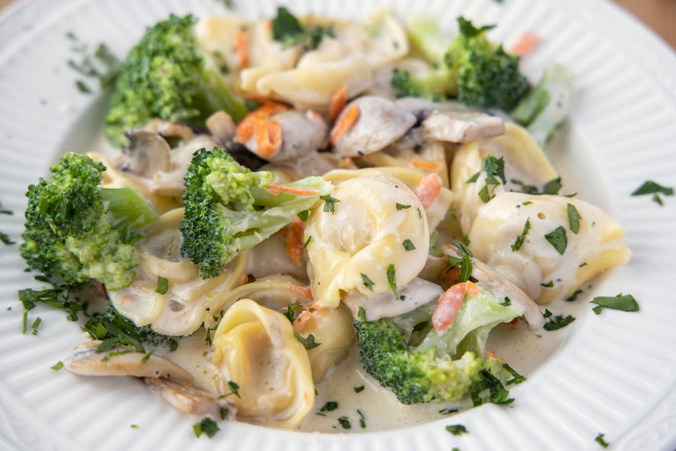 broccoli tortellini alfredo in a white bowl.