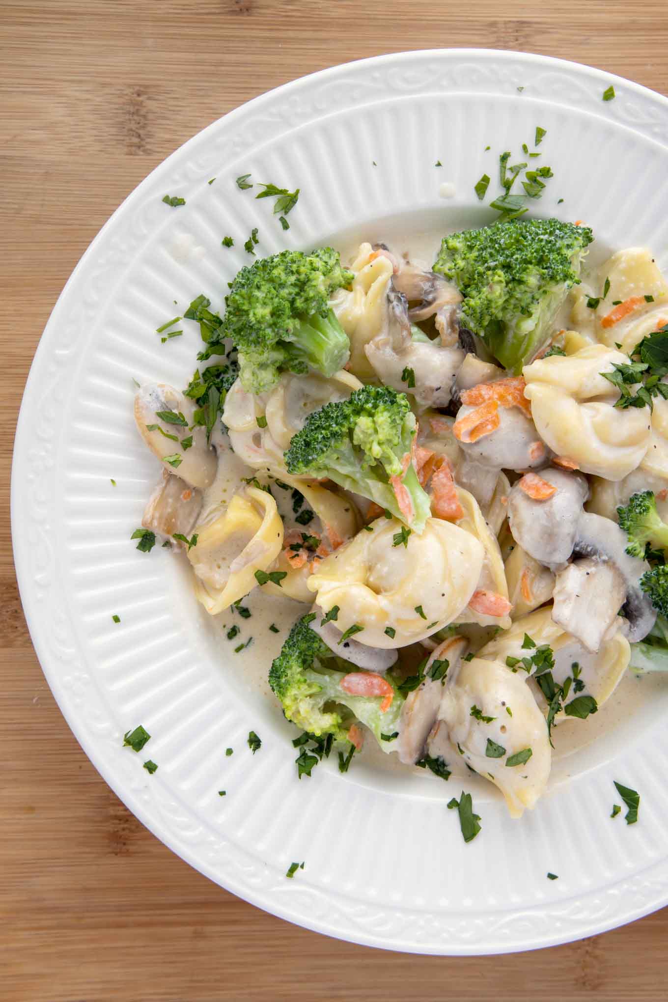 overhead  shot of white bowl with broccoli tortellini alfredo.