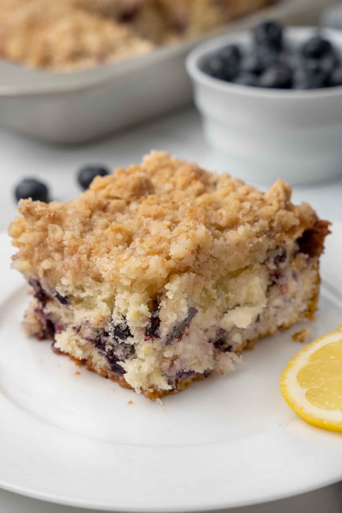 slice of blueberry buckle on a white plate with blueberries in the background