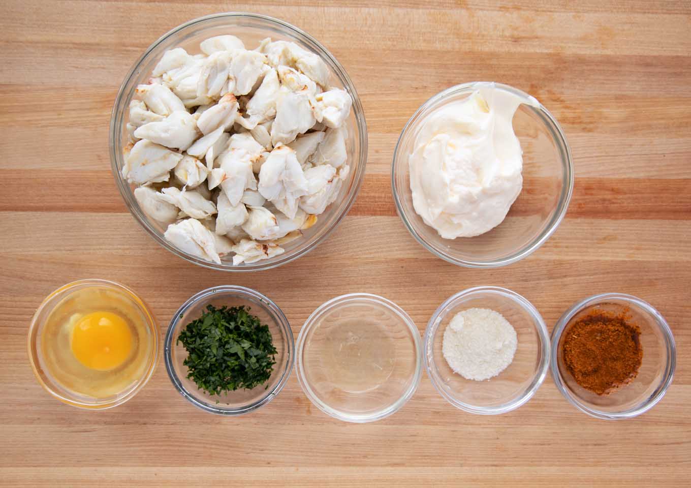 ingredients to make crab imperial in glass bowls on a cutting board