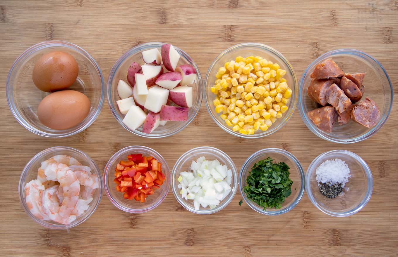 ingredients to make a low country breakfast in glass bowls on a wooden cutting board