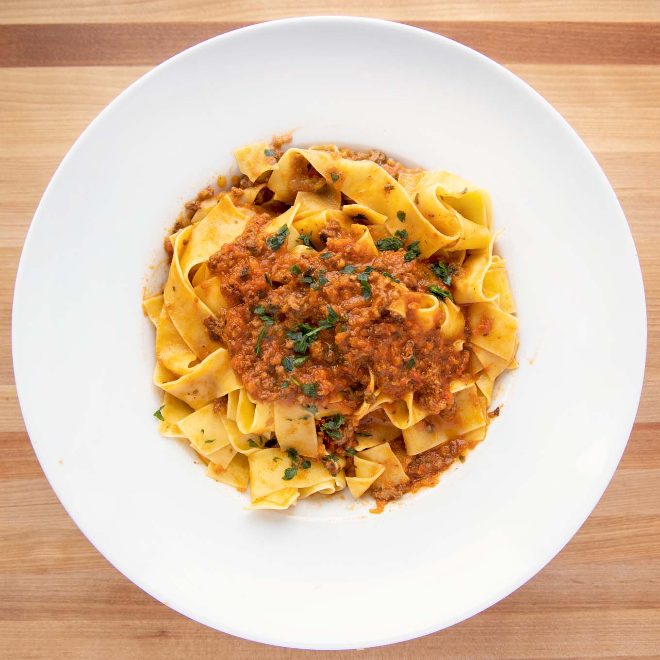 overhead shot of a white bowl with pappardelle bolognese