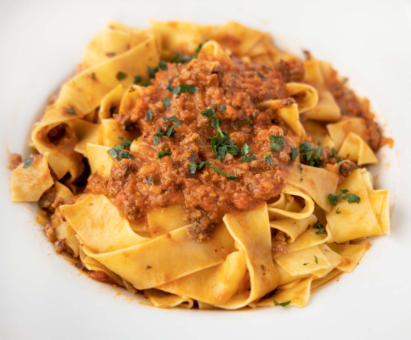white bowl of pappardelle noodles with bolognese sauce