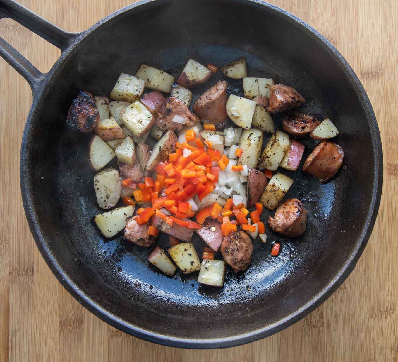 cast iron skillet with potatoes, andouille sausage, peppers and onions with a little smoke coming off the pan