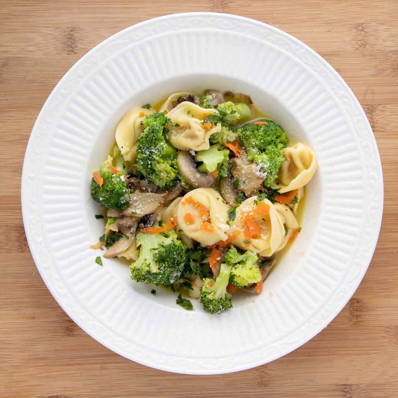 broccoli tortellini with broth in a white bowl.
