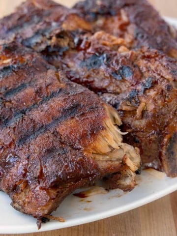 3 half racks of grilled baby back ribs on a white platter